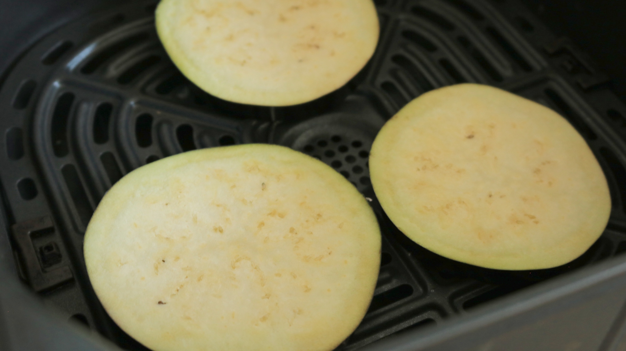 Freshly sliced eggplant in an air fryer basket.