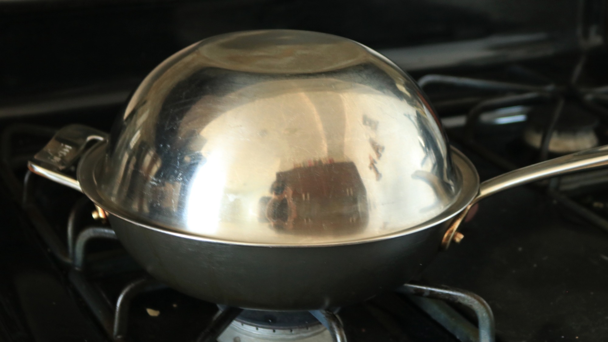 A frying pan with an upside-down metal bowl on top.