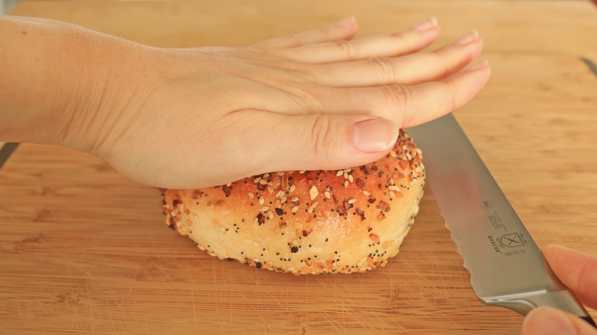 Hand pressing bagel on table and knife next to the bagel